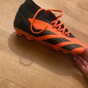 Adidas Predator orange fotbollsskor - Säljer ett par Adidas Predator fotbollsskor i orange och svart med snörning och högre strumpliknande skaft. Skorna har mönstrad ovandel och robust dobbsula för gräsplan. Perfekta för dig som vill sticka ut på planen.