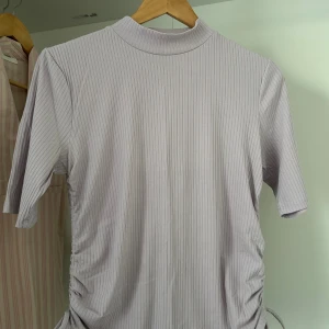 Ljuslila ribbad polotopp från Lindex - Säljer en ljuslila ribbad polotopp från Lindex i storlek M. Toppen har korta ärmar, hög krage och snygg snörning på sidorna som ger en cool detalj. Materialet är mjukt och stretchigt, perfekt för dig som gillar en chill och trendig look.