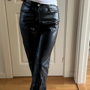 Svarta raka byxor i skinnimitation - Snygga svarta byxor i skinnimitation med raka ben och klassisk femficksmodell. Byxorna har normal passform och stängs med dragkedja och knapp. Perfekta för dig som vill ha en edgy look med stilren vibe. Aldrig använda 