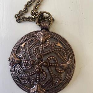 Kalevala bronsfärgat halsband med mönster - Kalevala fint smycke! Unikt halsband med rund, bronsfärgad medaljong och detaljerat flätat mönster i keltisk stil. Kedjan är grov och matchar medaljongens antika look. Märkt 'Made in Finland' på baksidan. Perfekt för dig som gillar statement-smycken med retrovibbar.  