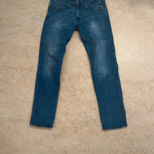 Replay Anbass Slim Fit Jeans Blå - Säljer ett par blå Replay Anbass jeans i slim fit med klassisk femficksdesign och snygga slitningar på både fram- och baksida. Jeansen har raka ben och är tillverkade i mjukt denimtyg som sitter skönt hela dagen.