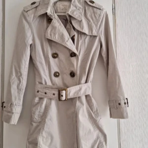Beige trenchcoat 2000s - Stilren beige trenchcoat från Stradivarius med klassisk dubbelknäppning, axelklaffar och bälte i midjan, ända gjort från italien, det passar även dig som är S o XS💕