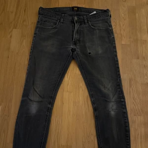 Mörkgrå skinny jeans från Lee ”Luke” - Säljer ett par mörkgrå skinny jeans från Lee ”Luke” med slitningar och små hål på framsidan. Jeansen har klassisk femficksdesign, svarta detaljer och en snygg tvättad look. Perfekta för dig som gillar en lite tuffare stil.