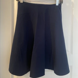 GANT Mörkblå kjol, storlek 36 - Enkel och stilren mörkblå kjol från GANT i storlek 36. Kjolen har en klassisk A-linjeform och är knälång, vilket ger en snygg och tidlös siluett. Perfekt att matcha med en stickad tröja eller en skjorta för en clean look.