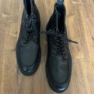 Svarta boots med snörning - Stilrena svarta boots  med snörning och dragkedja på sidan för enkel påtagning. Grov sula med bra grepp och rund tå. Insidan har ett rutigt foder som ger extra känsla. Perfekta för höst och vinter när du vill ha både stil och funktion. OBS innersulan i båda skorna saknas.
