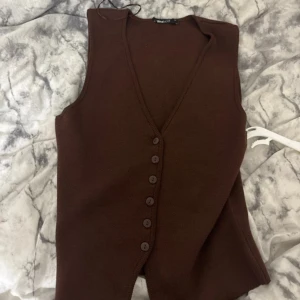 Brun stickad väst med knappar - Snygg brun stickad väst från Weekday med v-ringning och knappar framtill. Västen har en klassisk passform och är perfekt att styla över en skjorta eller t-shirt. Enkel och stilren design som funkar till många outfits.