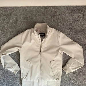 Beige jacka i XS - Snygg beige jacka från Dressmann i storlek XS. Jackan har ribbade muddar, två snedställda fickor och dragkedja framtill. Ståkrage med tryckknappar och stilren design som passar till många olika looks. Köpte jackan för 999kr och den är i princip oanvänd. Mitt pris 399kr🤩Skriv privat om fler bilder önskas.