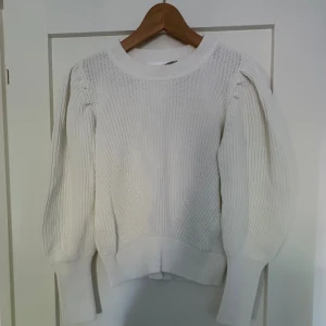 Vit stickad tröja med puffärm - Säljer en vit stickad tröja med breda muddar och snygga puffärmar. Tröjan har rund halsringning och ett ribbat mönster som ger en stilren look. Perfekt för lager-på-lager under kyliga dagar.