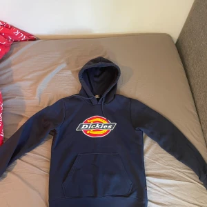 Mörkblå Dickies hoodie med logga - Säljer en mörkblå hoodie från Dickies i storlek S. Tröjan har stor Dickies-logga framtill, huva med snörning och en klassisk känguruficka. Perfekt för dig som gillar streetwear och vill ha en enkel men snygg look.