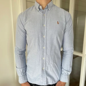 Polo Ralph lauren skjorta  - Säljer denna riktigt snygga ljusblåa Ralph lauren skjorta! Den är i bra skick enda defekten är att den är något gul i armhålorna men det är inget som syns när man har på sig den, storlek S modell slim fit, 72 cm lång och 46 cm bred under armhålorna, jag på bilden är 184 cm och väger 82 kg, hör gärna av dig vid frågor!