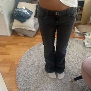 Svarta bootcut jeans med låg midja - Säljer ett par svarta jeans med bootcut-modell och låg midja. Jeansen har klassiska fem fickor, dubbla knappar och en snygg tvättad finish. Perfekta för dig som gillar en avslappnad men ändå trendig look.
