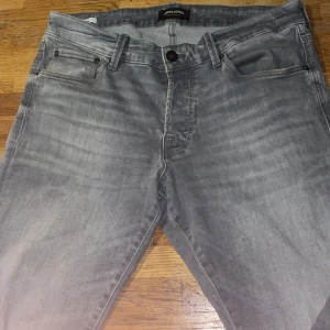 Grå slim fit jeans Jack & Jones 34/32 - Slim fit jeans från Jack & Jones i en snygg grå tvätt. Modellen heter Glenn och har klassisk femficksdesign, dragkedjegylf och diskreta sömmar på bakfickorna. Perfekta för dig som gillar en smalare passform och stilren look.