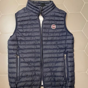 Mörkblå dunväst från Colmar - Snygg mörkblå dunväst från Colmar med quiltad design och dragkedja framtill. Västen har två fickor med dragkedja och en hög krage. Perfekt för lager-på-lager och har en sportig vibe med Colmar-logga på bröstet.