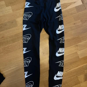 Nike leggings XS med logotyptryck - Svarta leggings från Nike i storlek XS med stora vita Nike-loggor tryckta längs hela benen. Elastisk midja med texten 'JUST DO IT.' på insidan.