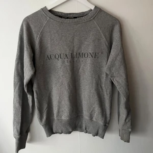 Grå sweatshirt från Acqua Limone - Säljer en grå sweatshirt från Acqua Limone med klassisk logga tryckt på bröstet och citrongul broderad detalj i nacken. Tröjan har rund hals, ribbade muddar och är tillverkad i mjuk bomullsmix. Perfekt för chill dagar och enkel att matcha med jeans eller joggers.
