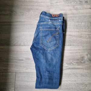 Blå jeans från Dondup - Säljer ett par klassiska blå jeans från Dondup med snygga kontrastsömmar och ikonisk logga på bakfickan. Jeansen har rak passform och normal midja, tillverkade i slitstarkt bomullsjeans. Perfekta för dig som gillar stilrena och tidlösa jeans.