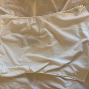 Vit bandeau tubtopp från 157 - Säljer en stilren vit bandeau tubtopp från 157. Toppen är axelbandslös och har en enkel, clean design i mjuk bomull. Perfekt att matcha med jeans eller kjol för en fräsch look. Storlek L. Helt ny med prislapp på