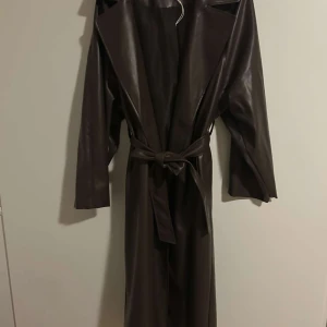 Brun skinn trenchcoat - Säljer en lång, mörkbrun trenchcoat från NA-KD.  För liten, använt max 7-8 gånger strlk 38