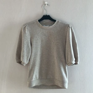 Beige puffärm tröja från 157 - Beige tröja från 157 med puffiga korta ärmar och rund halsringning. Mjuk och skön känsla, perfekt för dig som gillar en enkel men trendig look. Passformen är normal och materialet känns som bomullsmix. Säljes pga av utväxt 