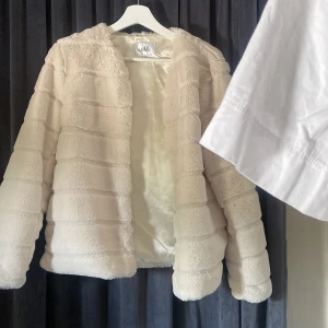 Beige pälsjacka från Isolde, stl 38 - Supermjuk och fluffig beige pälsjacka från Isolde i storlek 38. Jackan har horisontella sömmar som ger en cool struktur och är helfodrad med glansigt tyg. Perfekt för dig som vill ha en mysig och trendig look under kyliga dagar.