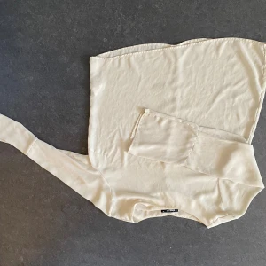 Beige blus - Säljer en stilren offwhite tubtopp från Zara med lång ärm på ena sidan för en cool asymmetrisk look. Toppen är axelbandslös och har en slät, mjuk yta som känns lyxig. Perfekt för dig som vill sticka ut med en unik och trendig topp.
