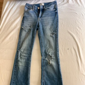 Ljusblå bootcut jeans från ONLY - Säljer ett par ljusblå jeans från ONLY i bootcut-modell med slitna detaljer och hål på benen. Jensen är låg/medium midjade, jag stylade då dessa oftast med en overzised eller längre tröja. 