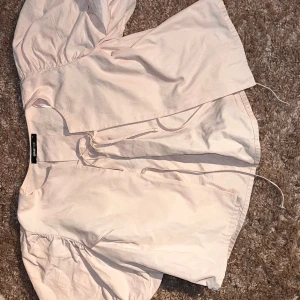 Ljusrosa omlottblus från Gina Tricot - Supersöt ljusrosa omlottblus från Gina Tricot med puffiga ärmar och knytband framtill. Blusen har en luftig passform och är perfekt för vår och sommar. Tillverkad i mjuk bomull som känns skön mot huden.