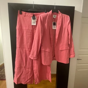 Rosa linnékostym Twist & Tango stl 38/40 - Säljer en snygg rosa kostym från Twist & Tango i 100% linne. Setet består av en kavaj med fickor och en rak, hellång byxa med resår i midjan. Perfekt för dig som gillar färg och vill sticka ut med en fräsch look. Båda plaggen har etiketter kvar.