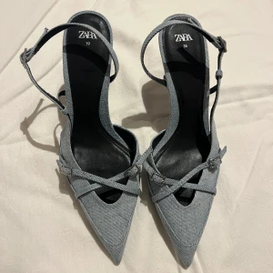 Blå jeanspumps med spetsig tå från Zara - Snygga pumps från Zara i blått jeanstyg med spetsig tå och smala remmar med små spännen. Storlek 39, i fint skick.