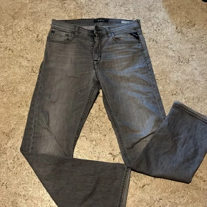 Grå Replay jeans barn  - Snygga grå jeans från Replay med klassisk femficksdesign och raka ben. Jeansen har diskreta slitningar och svarta detaljer vid fickorna. Perfekta för dig som gillar en stilren look med lite edge. Materialet är mjukt och följsamt jeans.