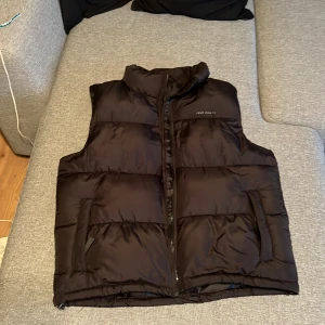 Svart dunväst från True North - Snygg svart dunväst från True North med krage och dragkedja framtill. Västen är quiltad och har praktiska fickor på sidorna samt en innerficka med dragkedja. Tillverkad i 100% polyester, perfekt för lager-på-lager under kyliga dagar.