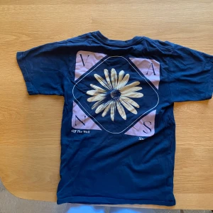 Mörkblå Vans t-shirt med blomtryck - Snygg mörkblå t-shirt från Vans med stort blommotiv på ryggen och diskret Vans-logga på bröstet. Klassisk rund hals och korta ärmar. Materialet är mjuk bomull som känns skönt mot huden. Perfekt för dig som gillar streetwear och coola prints.