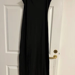 Svart långklänning från Elam W - Enkel och stilren svart långklänning från Elam W. Klänningen har en rak passform, ärmlös design och rund halsringning även har öppning på på en av sidorna. Perfekt för dig som gillar minimalistisk stil och vill ha en klassisk look. Storlek är L men passar bättre för M. Den är helt ny och kommer från rök- och djurfritt hem. 