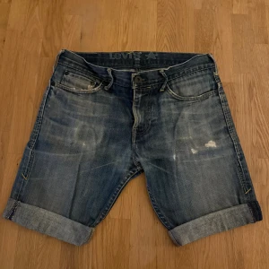 Levi's jeansshorts ”Blue Star” med uppvik - Säljer ett par klassiska blå jeansshorts från Levi's ”Blue Star” med snyggt uppvikta ben och slitna detaljer. Shortsen har fem fickor, knapp och dragkedja framtill samt Levi's logga på bakfickan. Perfekt för dig som gillar en avslappnad och cool stil.