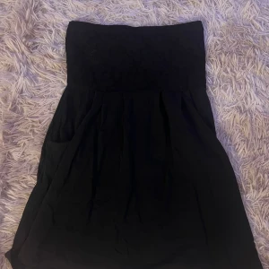 Svart axelbandslös klänning Vero Moda - Svart axelbandslös kortklänning från Vero Moda i storlek S. Överdelen har en fin spetsdetalj och kjolen är lätt utställd. Perfekt för dig som gillar en enkel men ändå elegant look.