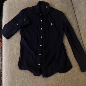 Mörkblå skjorta från Polo Ralph Lauren - Snygg mörkblå skjorta från Polo Ralph Lauren med klassisk krage och vita knappar. Säljer denna då den börjar bli lite liten på mig, jättebra skick annars med inga fläckar eller liknande. Nypris va runt 2000kr mitt pris 650 vilket låter rätt så bra, priset kan diskuteras.