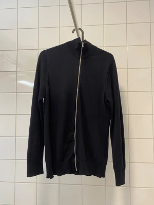 Mörkblå merinoullskofta från Riley (fullzip) - Säljer en mörkblå kofta från Riley i mjuk merinoull. Koftan har hel dragkedja framtill, hög krage och lång ärm. Perfekt för lager på lager och riktigt clean look. Passar dig som gillar stilrena plagg med premiumkänsla. Obs liten i storleken, passar xs