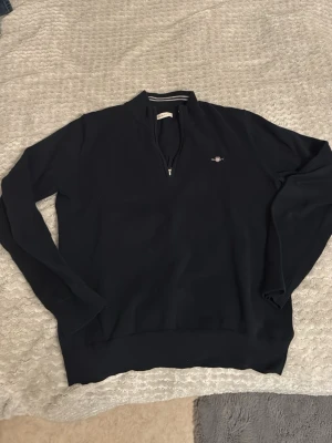 Marinblå half zip tröja från GANT - Snygg marinblå långärmad tröja från GANT med half zip och broderad logga på bröstet. Klassisk ståkrage med vita ränder på insidan ger en clean look. Perfekt till både jeans och chinos för en stilren vibe.