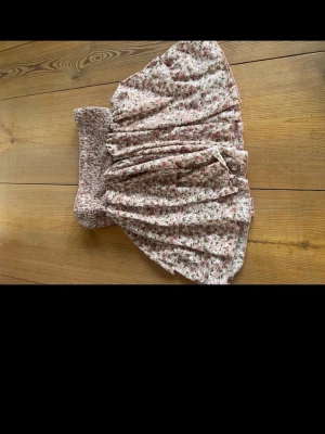 Rosa blommig kortkjol från SHEIN - Supersöt rosa kortkjol från SHEIN med blommigt mönster och smockad midja. Kjolen har volanger och är gjord i ett lätt och luftigt material, perfekt för varma dagar. Färgerna går i ljusrosa med inslag av grönt och vitt.