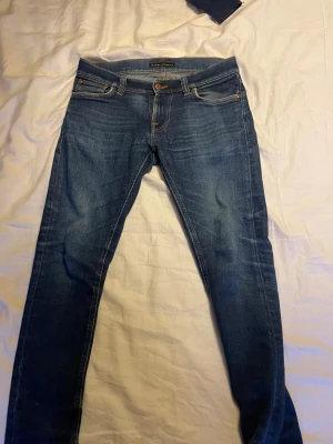 Nudie jeans - Snygga blå jeans från Nudie Jeans med klassisk orange söm på bakfickorna. Modellen är slim fit med smal passform och normal midja. Jeansen har slitningar på ena benet och är tillverkade i mjukt denimtyg. Nu pris runt 1600