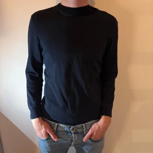 Mörkblå tröja från Bläck, storlek M - En stilren mörkblå tröja från Bläck i storlek M. Tröjan har rund halsringning och långa ärmar, perfekt för lager-på-lager. Materialet känns mjukt och passar bra till jeans.