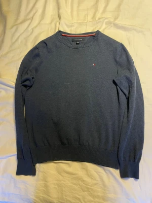  Stickad tröja Tommy Hilfiger - Snygg marinblå stickad tröja från Tommy Hilfiger i storlek XS. Klassisk rund halsringning och diskret logga broderad på bröstet. Tröjan har långa ärmar och ribbade muddar vid ärmslut och nederkant. Perfekt för dig som gillar stilrena plagg. Har en grå likadan som jag kan gå med på att sälja båda för 400