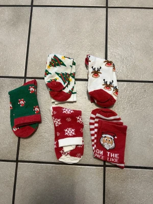 Juliga strumpor med mönster storlek 36-38 - Fem par färgglada julstrumpor med motiv som julgran, ren, snögubbe, snöflingor och tomte. Strumporna är i rött, grönt och vitt med roliga och festliga mönster, perfekta för att maxa julstämningen. Mjukt material som känns skönt på foten.