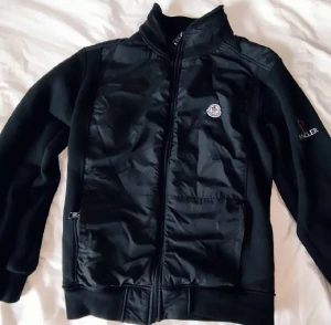Moncler jacka!!!! - PRIS KAN DISKUTERAS!!!!!.Svart bomberjacka från Moncler med glansig framsida och broderad logga på ärmen. Jackan har hög krage, hel dragkedja och två fickor mdragkedja. Materialmix med polyester och bomull ger en sportig och clean look.
