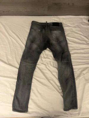 Grå Dsquared2 jeans, storlek 46 - Snygga grå jeans från Dsquared2 i storlek 46. Jeansen har en tvättad look med ljusare partier, klassiska fem fickor och svart Dsquared2-läderpatch bak. Materialet är bomull med lite stretch för skön passform. 