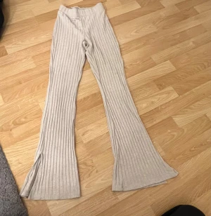 Beige ribbade bootcut byxor - Säljer ett par beige ribbade byxor med bootcut och slits vid benslut. De har hög midja och är gjorda i mjukt stickat material som är riktigt skönt. Perfekta för dig som gillar en chill och trendig look.