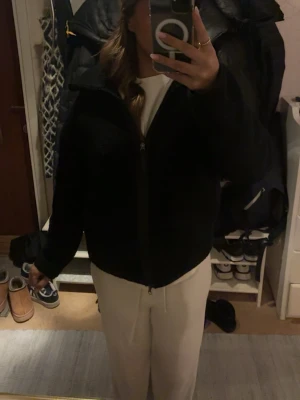 Svart teddyjacka med dragkedja - Mysig svart teddyjacka med hög krage och hel dragkedja framtill. Jackan har två stora runda fickor och är i en enkel, rak modell. Perfekt för kyliga dagar och ger en chill vibe till outfiten. Den är i xs men skulle påstå att den även passar för S/M