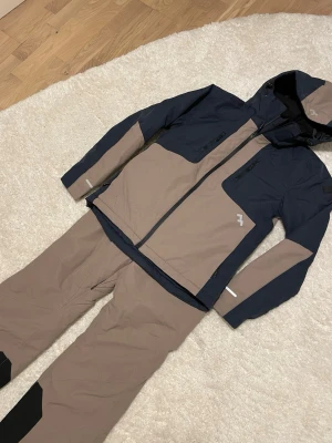 Beige skidbyxor och skidjackor med svarta och marinblå detaljer - Säljer jättefint skidställ, jättefin skidjacka och detsamma med skidjackan. Helt nyskick nypris 900kr för båda! XS på båda delarna. Beige svart marinblå färg. Samma beige på båda delarna däremot är de svarta detaljer på byxorna o marinblå detaljer på jackan.