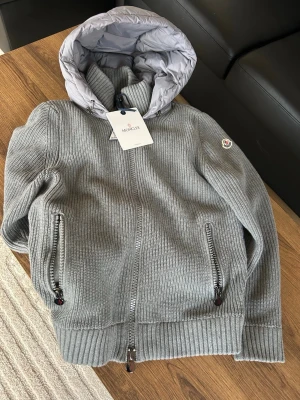 Moncler cardigan - Säljer en grå cardigan jacka från Moncler med stickade ärmar och ribbade muddar. Finns inga skador på den och använd ett fåtal gånger sen jag köpte den. Storleken är S men passar även M. Pris går att diskutera! Skriv för mer info.