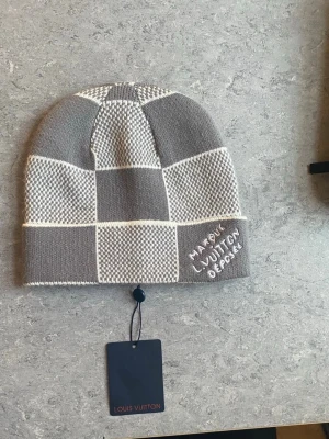 Grå-rutig Louis Vuitton mössa i kashmir - Säljer en exklusiv helt ny grå och vit rutig mössa från Louis Vuitton. Mössan är tillverkad i mjuk kashmir och ullblandning med inslag av silke. Broderad text 'Marque L. Vuitton Déposée' framtill. Snyggt rutmönster och diskret LV-tag på insidan. Pris kan ändras vid snabb affär.